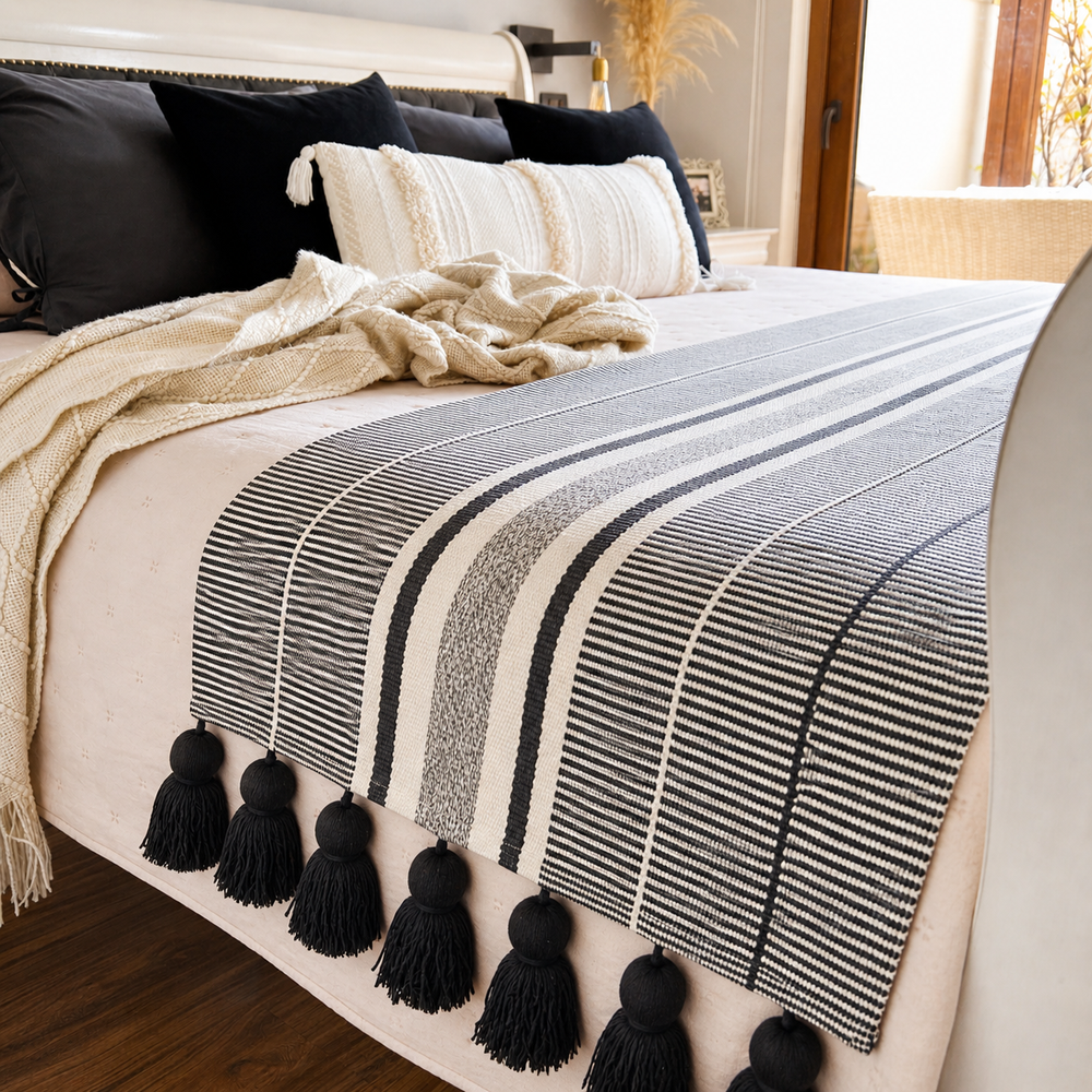 Piecera de cama blanca y negra con borlas decorativas sobre cama estilo nórdico