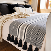 Piecera de cama blanca y negra con borlas decorativas sobre cama estilo nórdico