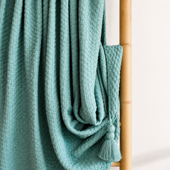 Manta decorativa verde agua con borlas sobre respaldo de madera ideal para sofá o cama